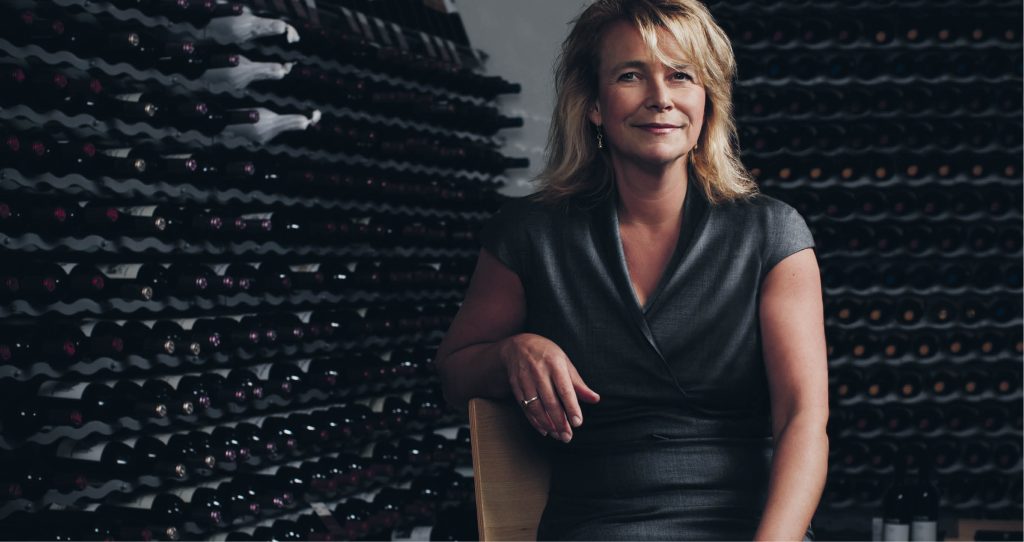 Magdalena Gerger, Systembolagets vd, med vinflaskor i bakgrund.