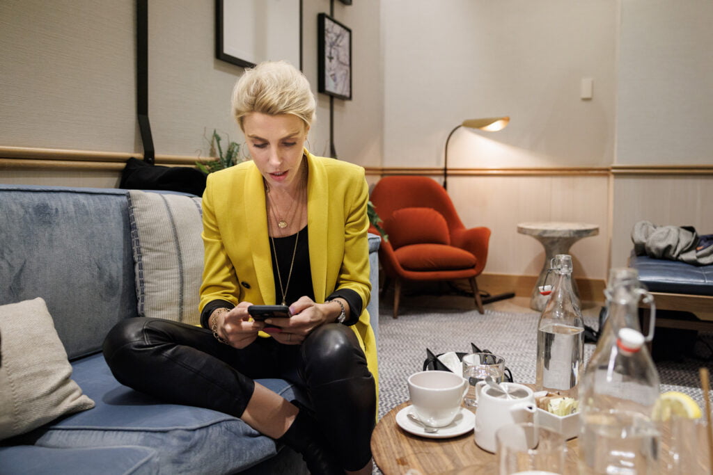 Clarissa Ward titta i hennes mobil. Sitter på en soffa och har på sig en gul kavaj och skinnbyxor.