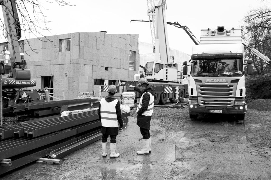 Byggarbetare utanför en nybygg med stor lastbil.