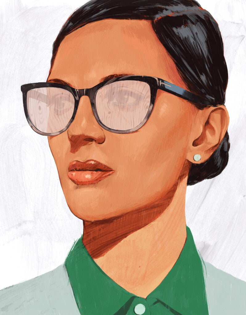 En professionell kvinna med glasögon, kammat hår och en örhängen. Hon har en grön skjorta på och svart hår.